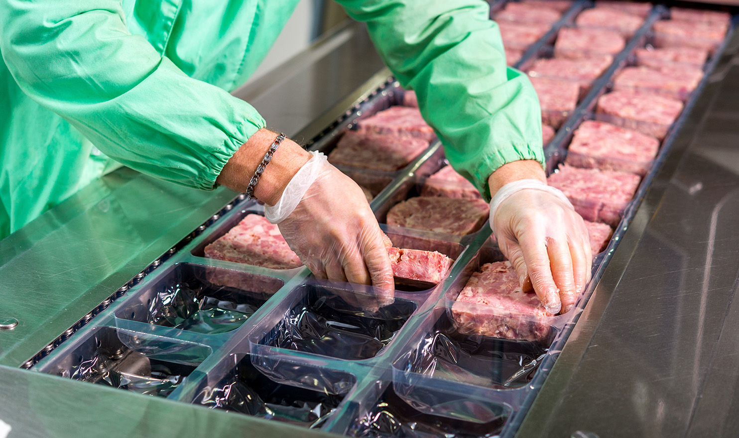 A pair of gloved hands are packaging ground meat into packaging. Food manufacturing insurance can help in cases where food gets someone sick.